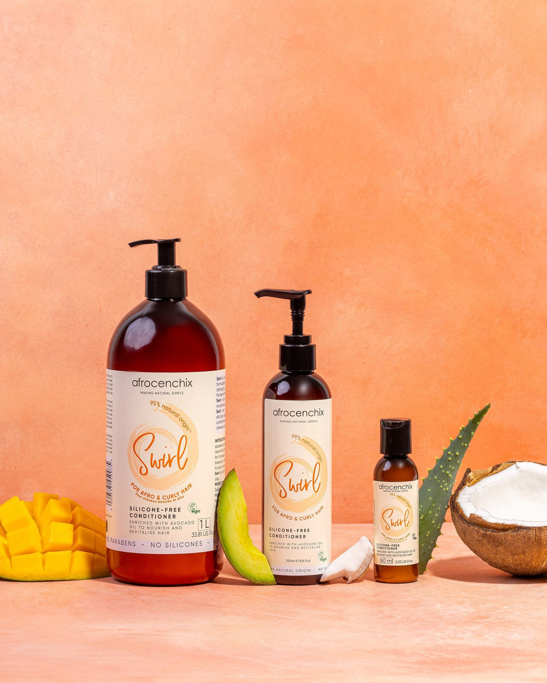 A range of hair care products from AfroChic, including a large bottle of silicone-free conditioner, a smaller bottle of a different product, and containers of hair oil and hair growth serum, displayed alongside natural ingredients like mango and coconut.