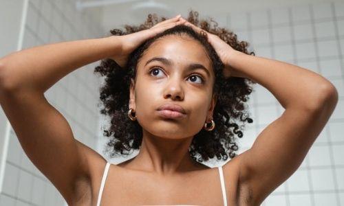 Afrocenchix 5 Easy Tips To Make Your Hair Routine More Eco-friendly: mixed woman holding her short curly hair in the bathroom