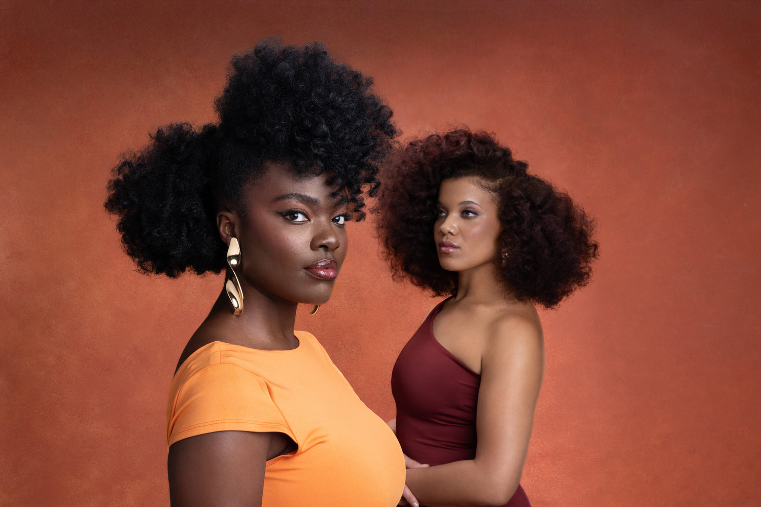 Two women with styled hair against a warm-toned background