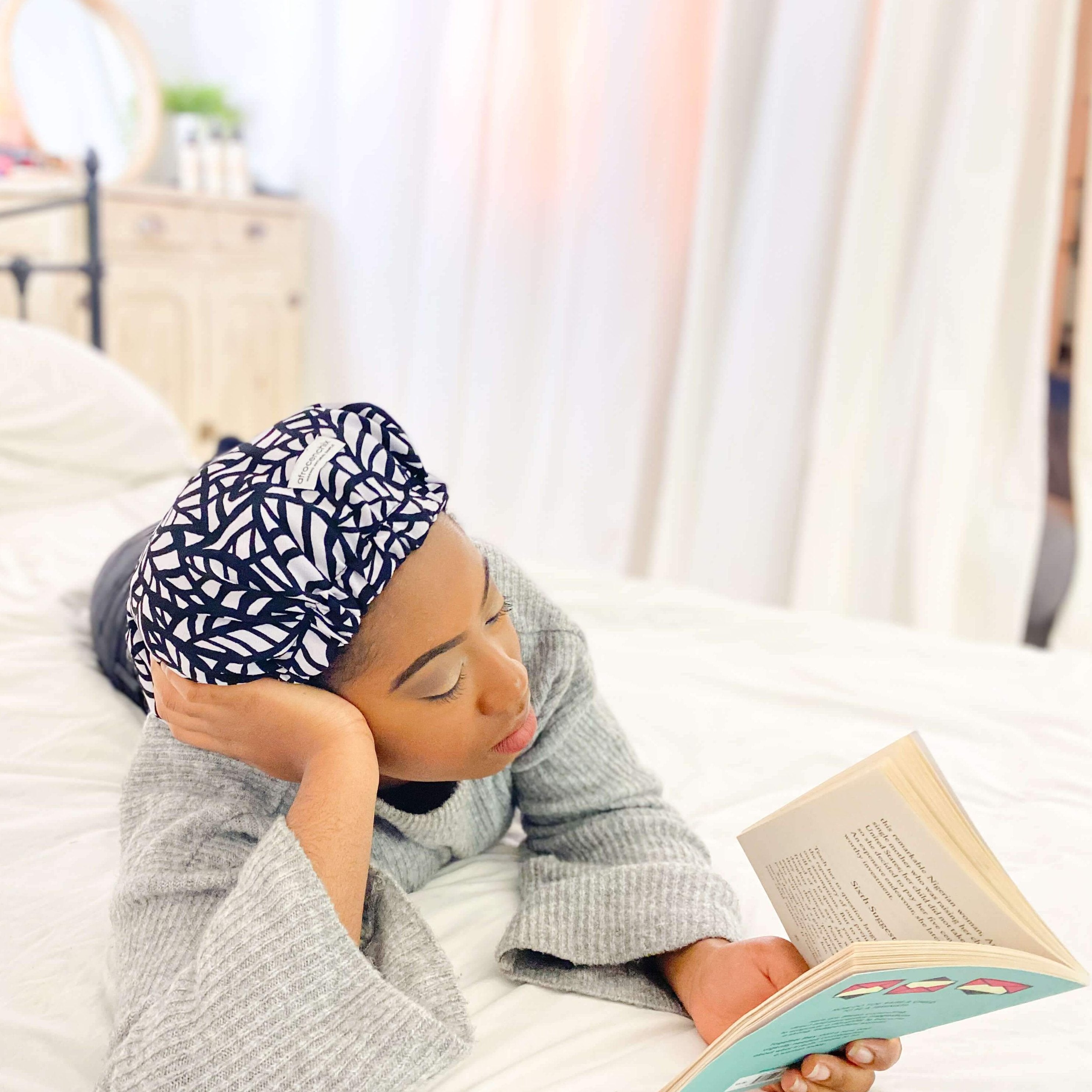 A person is lying down reading a book while wearing a floral print bonnet with satin lining on their head.