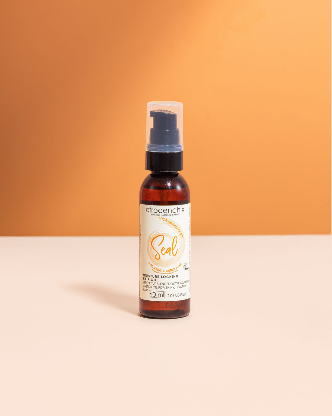 A bottle of Mini Seal - Natural Hair Oil with a spray nozzle, positioned against a orange and white background.