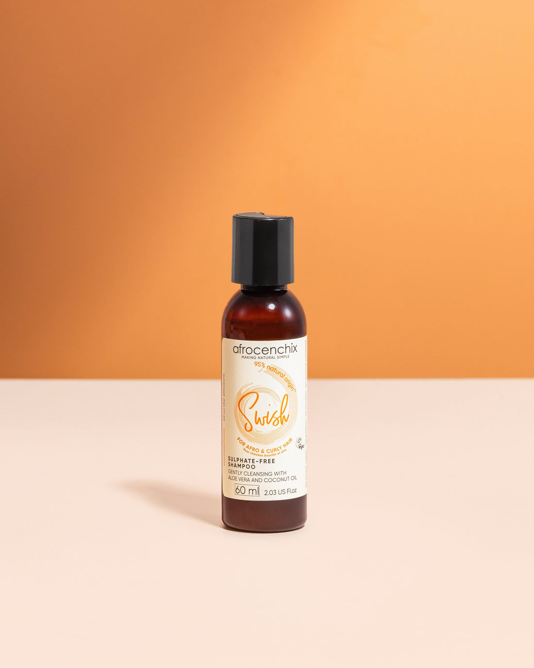 A bottle of Mini Swish - Sulphate-free Shampoo (60ml) positioned against an orange backdrop with a white surface, with the brand&