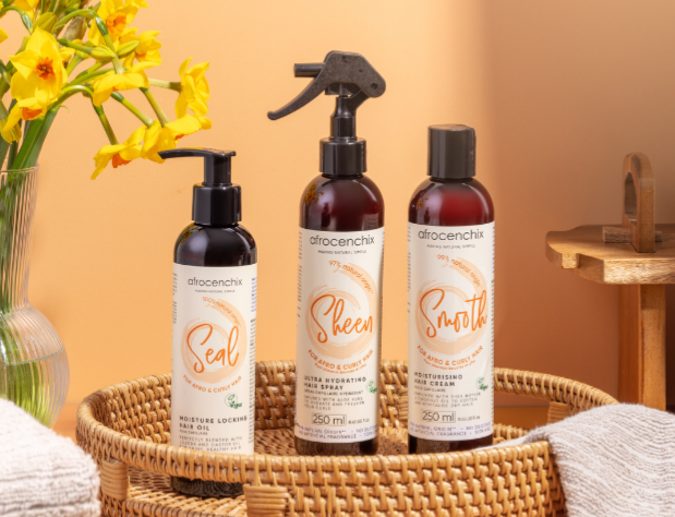 Three bottles of Africentrix hair care products in a basket with yellow flowers on an orange background